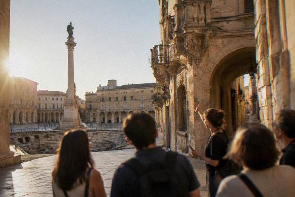 A guide pointing out carved balconies and an archway to a small group in a narrow lane, Piazza Sant'Oronzo, Lecce