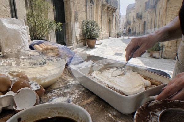 A worktop with eggs, flour and a tray of tiramisu being layered with a spoon, hands only, Centro Storico, Lecce