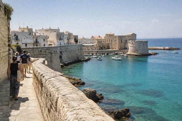 A small group of walkers on a coastal path along the ramparts above turquoise water, Otranto, Puglia
