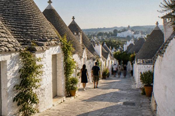 A small group of day visitors walking between rows of conical-roofed white stone trulli houses, Alberobello, Puglia