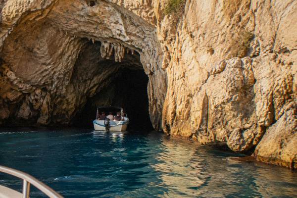 A small boat nosing into the dark mouth of a sea cave in a limestone cliff, Grotta Zinzulusa, Puglia