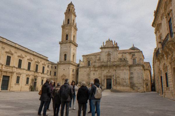 Small group listening to a guide in front of a Baroque church facade in Lecce