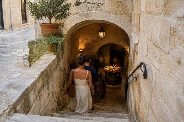 A small group going down a narrow stone stairway into a vaulted cellar where a tasting plate waits, Centro Storico, Lecce