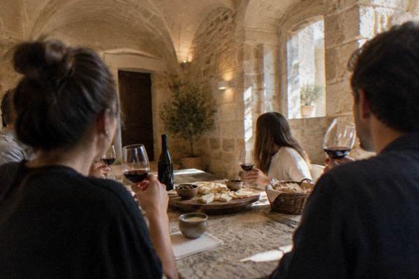 A small group tasting red wine and sliced cheese at a stone table in a vaulted old town room, Centro Storico, Lecce