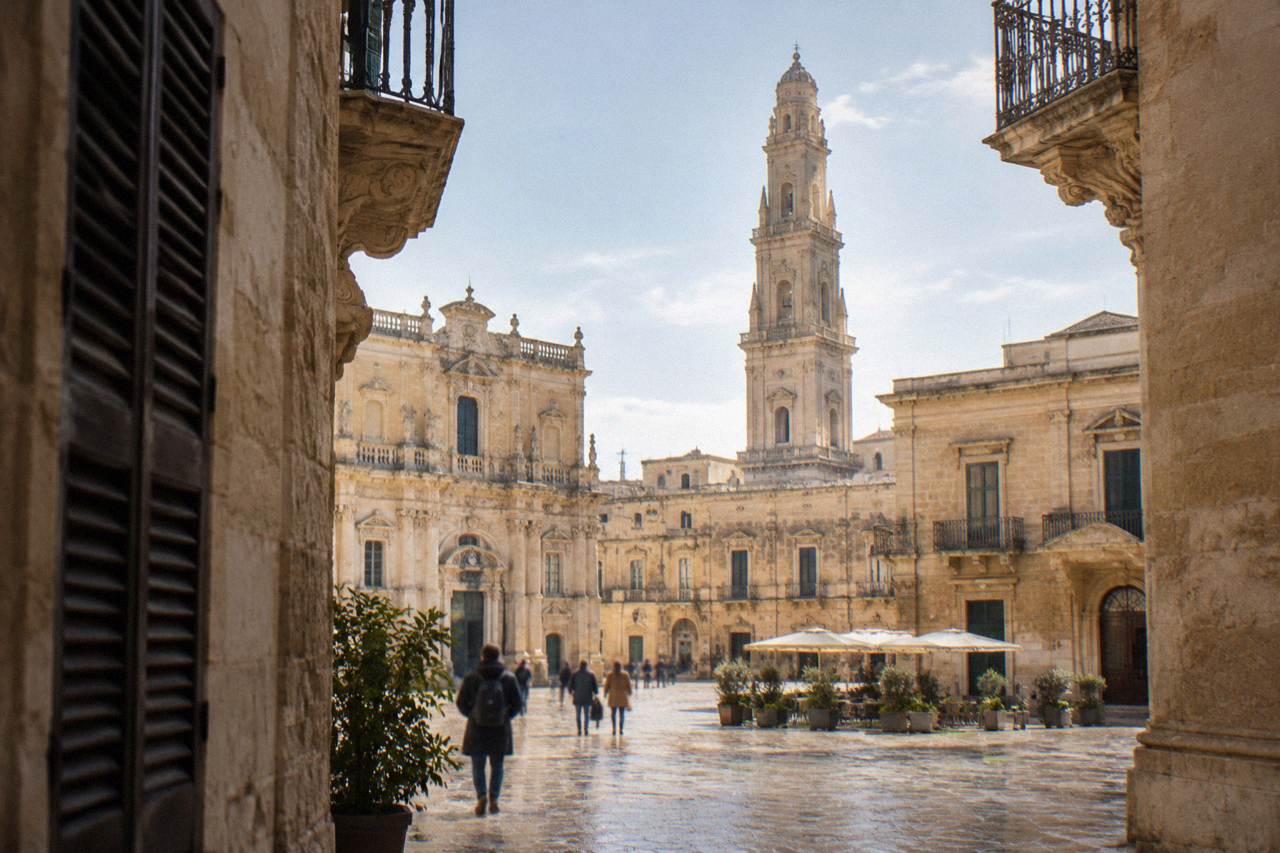 A sunlit square in Lecce with honey-coloured baroque facades and a tall bell tower