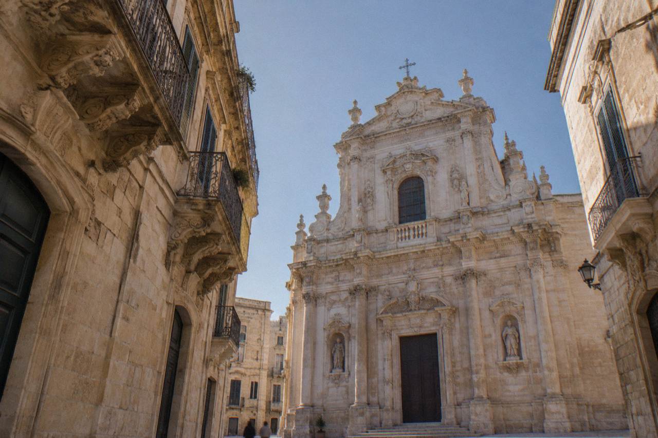 A honey-coloured baroque church facade in Lecce carved from pale limestone under a clear sky