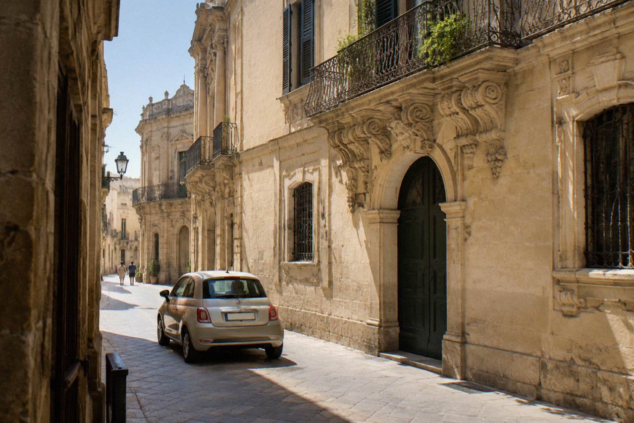 A narrow limestone street in Lecce's old town with a small car passing close to baroque buildings