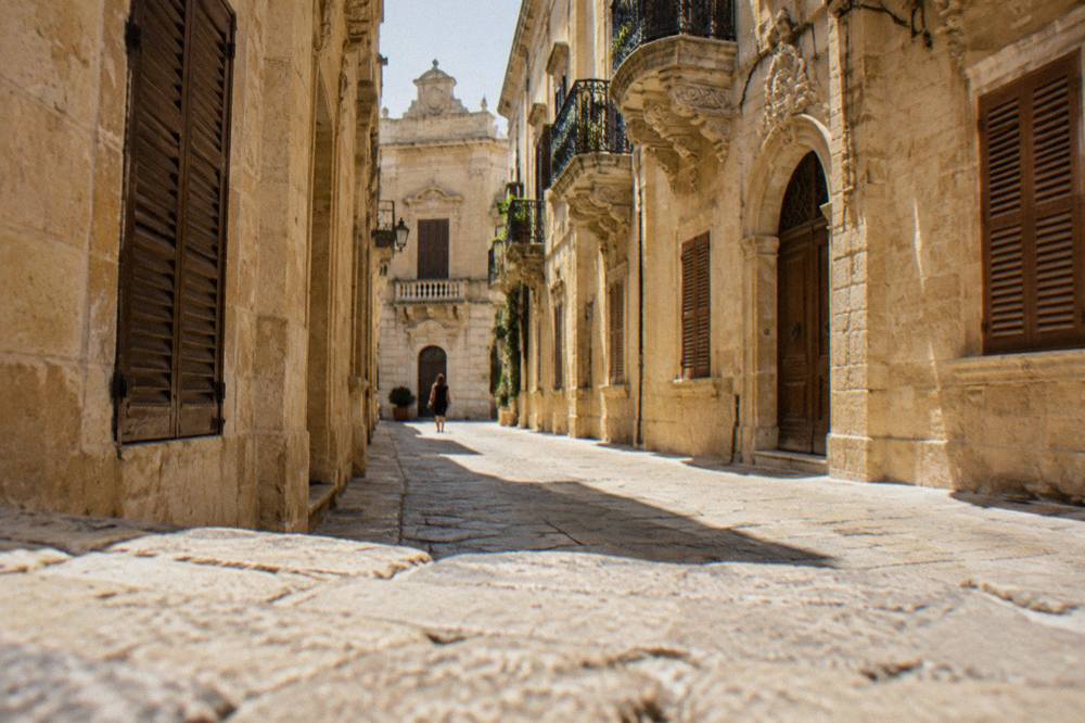 A narrow quiet alley in Lecce's old town with warm limestone walls and closed wooden shutters