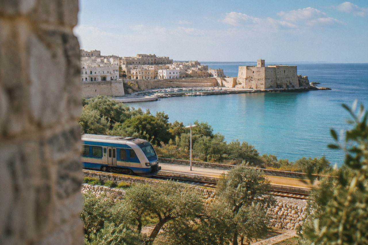 A regional train at a small southern Italian station surrounded by olive trees