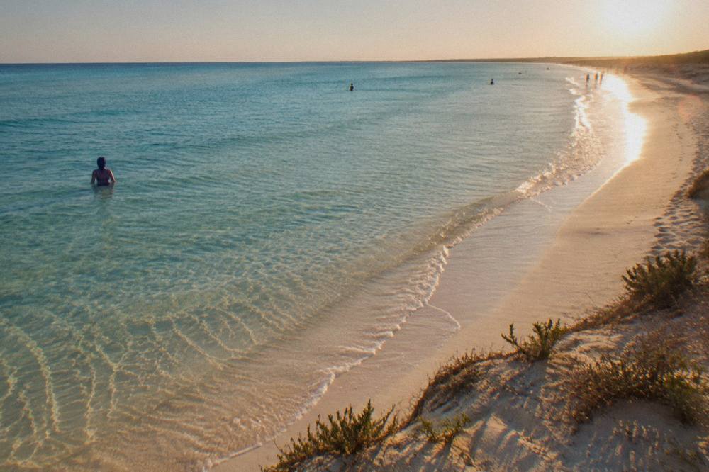 Turquoise shallow water over pale sand at a Salento beach in early evening light