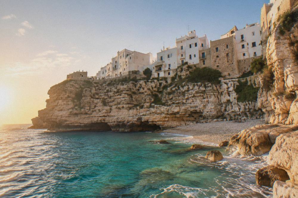 Turquoise water breaking on pale rocks below a small coastal town on the Salento coast