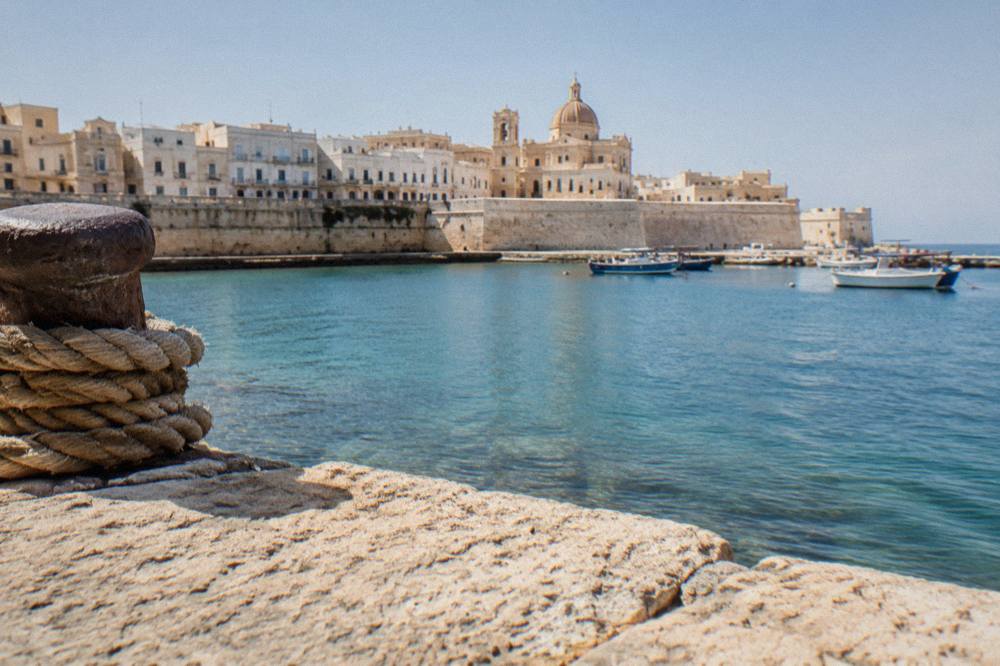 Gallipoli's old town on its island seen from the water, with pale buildings and a church dome above the harbour