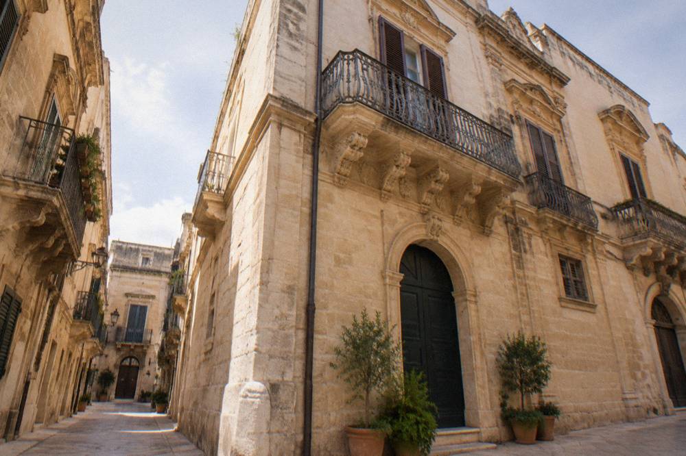 Sunlit stone street corner in Lecce with potted plants beside a doorway