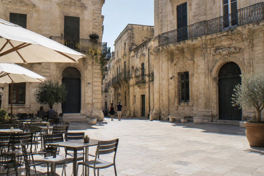A small square in Lecce with tables outside a bar and pale stone buildings
