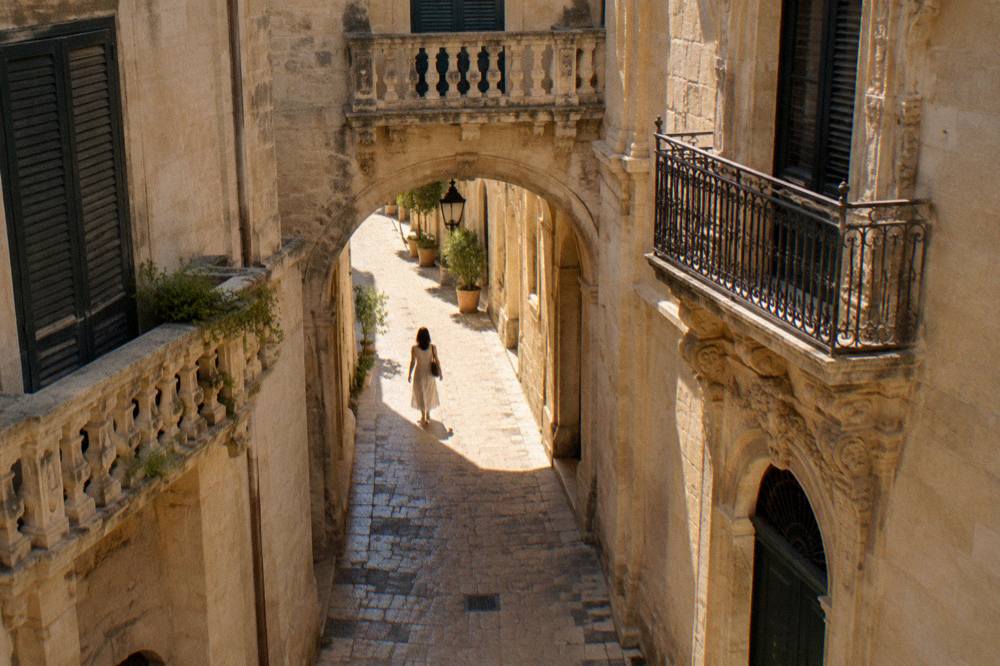 A quiet arched passageway between limestone buildings in Lecce at golden hour