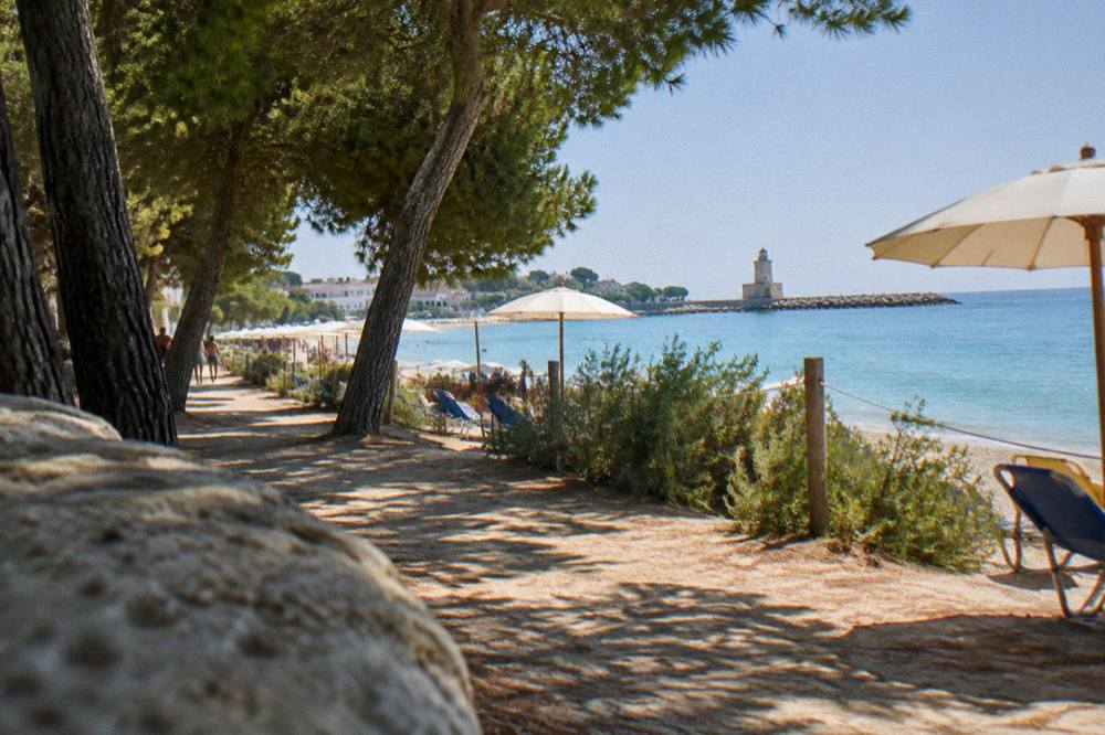 A pine shaded path between beach umbrellas and the sea at midday