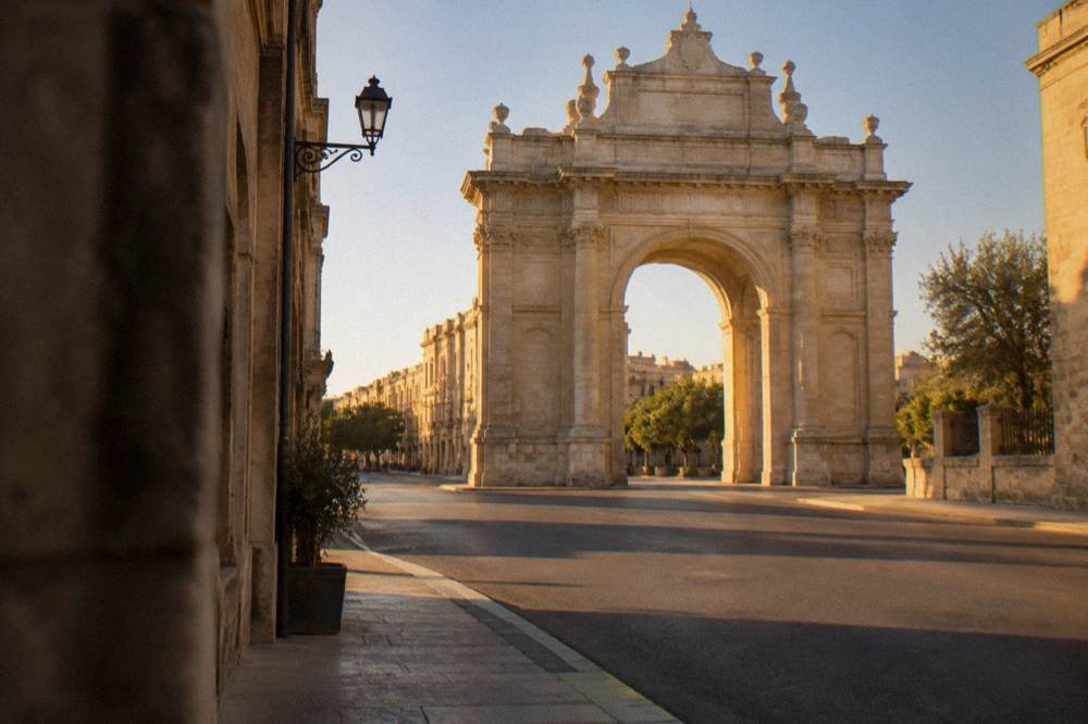 Stone city gate arch with a wide road beside it and no traffic in frame