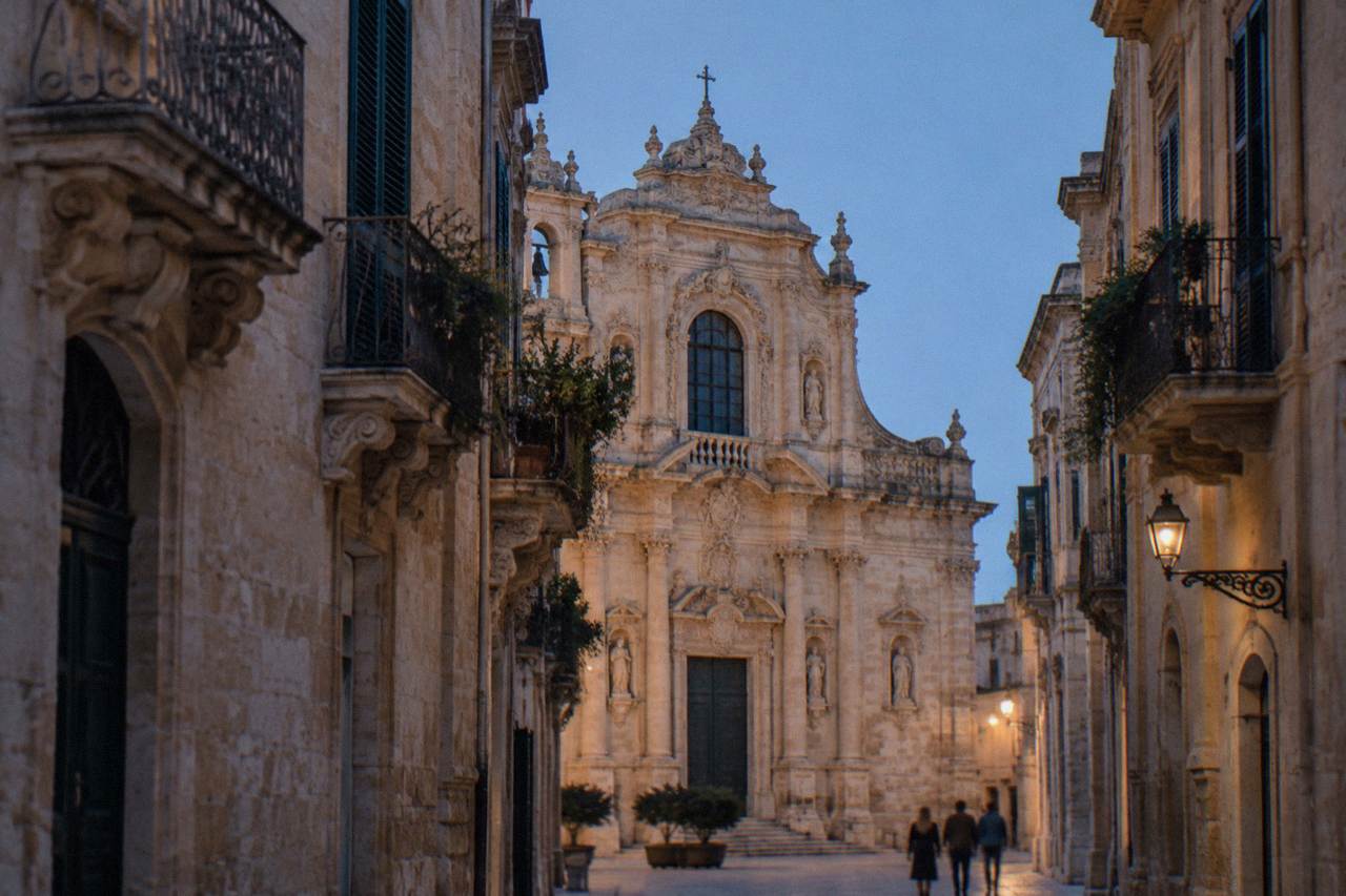 A baroque church facade in warm honey-coloured stone seen from a narrow Lecce street