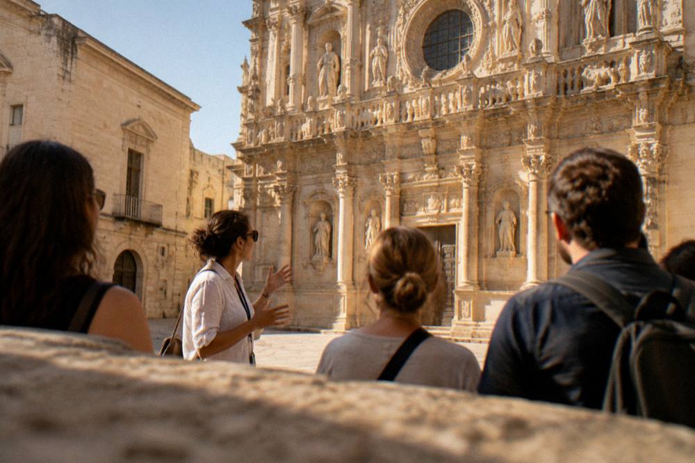 Guide speaking to a small group in a sunlit square of pale stone buildings