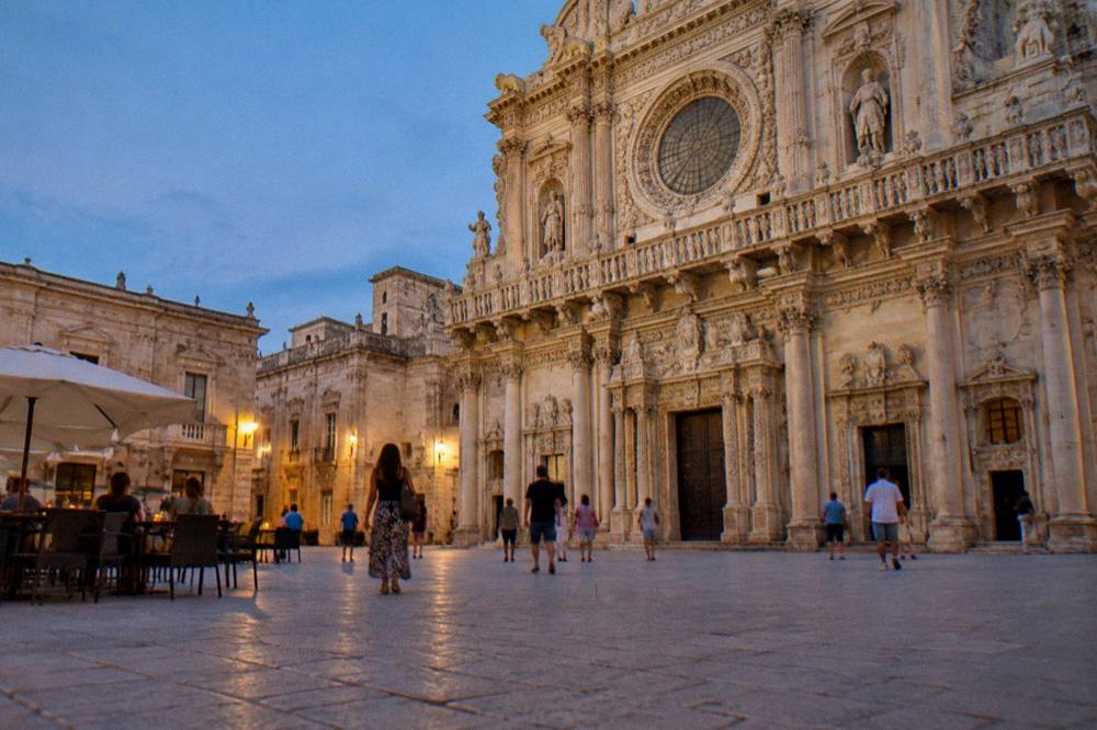 Evening light on a pale stone square with people walking and cafe tables