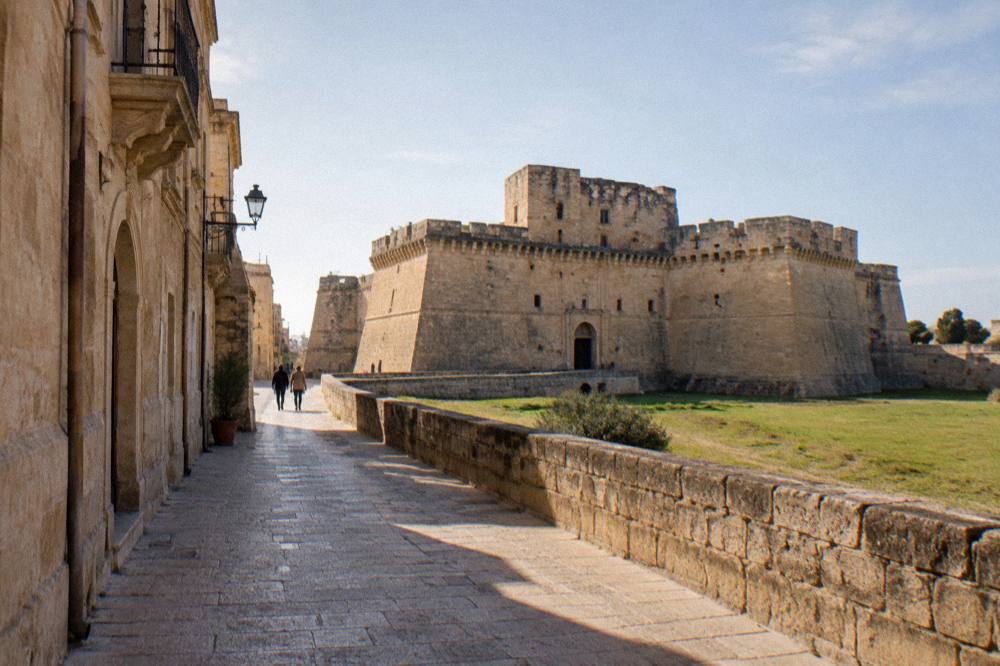 A quiet street of honey coloured stone buildings leading toward the castle in Lecce