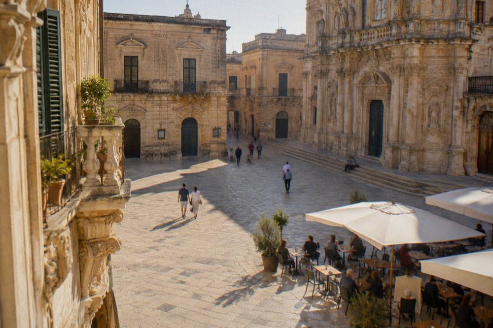 A sunny piazza in Lecce with baroque facades and people sitting at outdoor tables