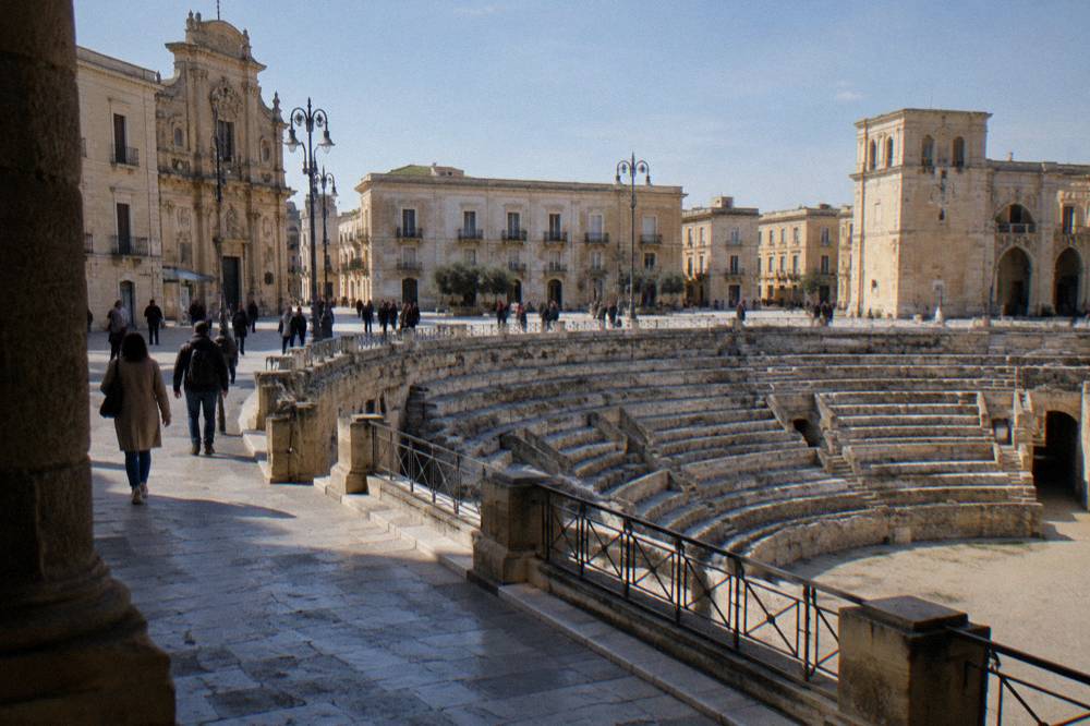Tourists and locals walking across Piazza Sant'Oronzo in Lecce beside the Roman amphitheatre remains