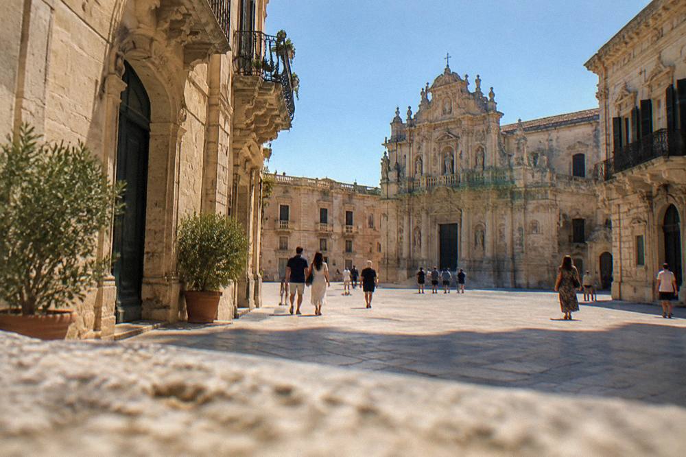 Sunlit piazza in Lecce with baroque facades and people walking