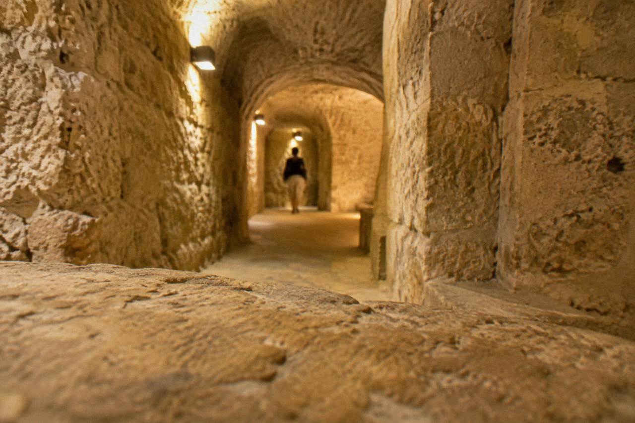 A narrow stone-walled underground chamber in a Lecce museum lit by warm electric light