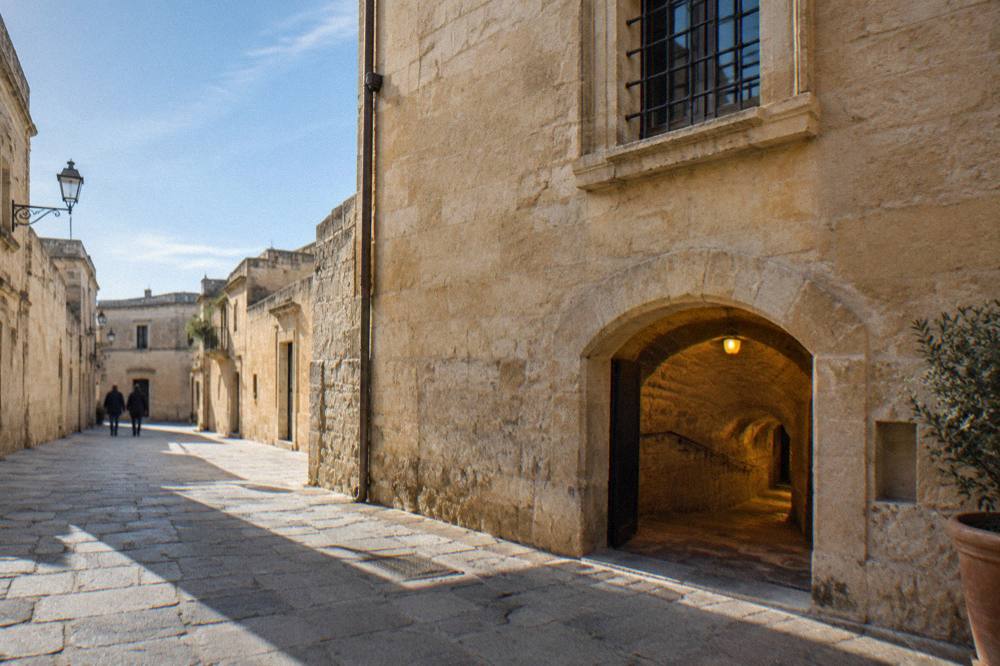 A low arched tunnel of pale stone lit by a single warm lamp in an underground museum