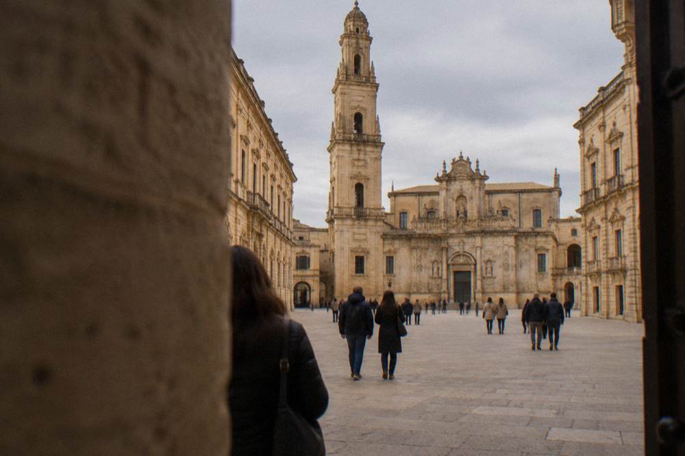 Tourists walking through the entrance arch into Piazza del Duomo in Lecce