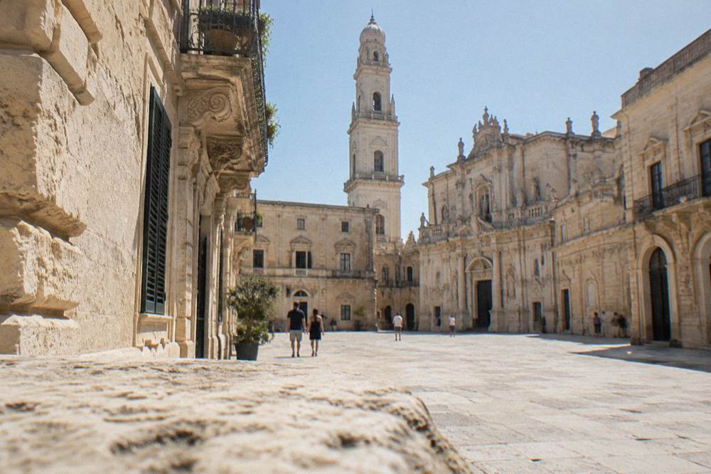 Enclosed limestone cathedral square with a tall bell tower and uniform Baroque facades