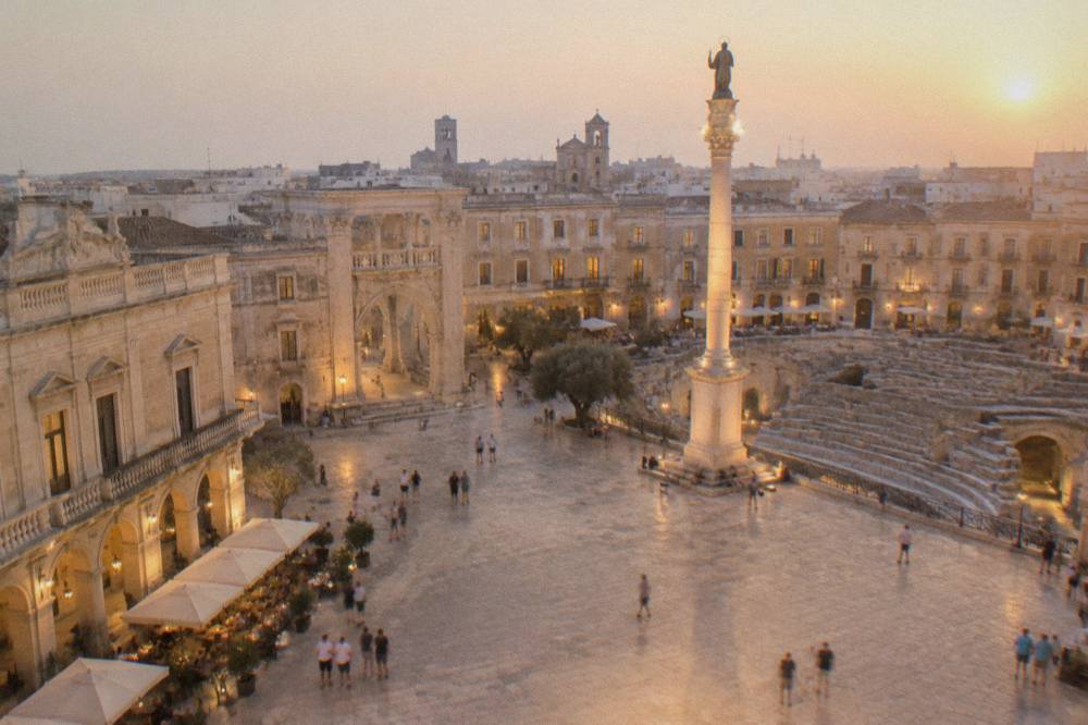 Evening view of the square with lit cafe tables, baroque facades and the illuminated column of Sant Oronzo