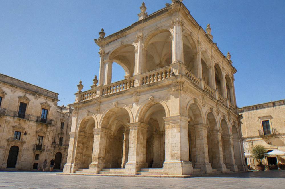 The arcaded loggia of the Sedile building with warm stone arches and a columned upper terrace