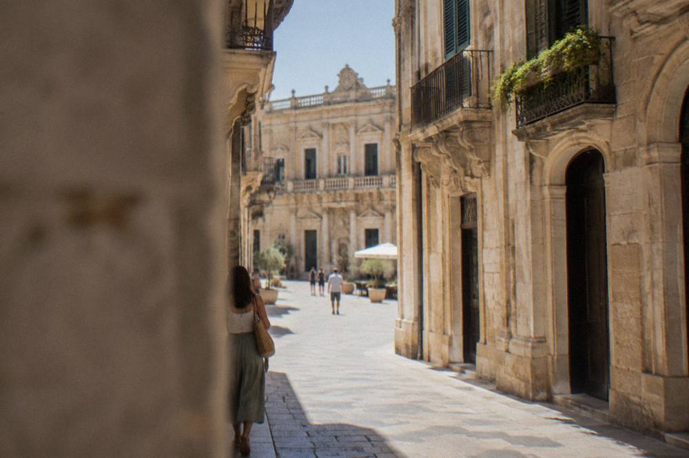 A narrow stone-paved street in Lecce's old town leading toward an open sunlit square