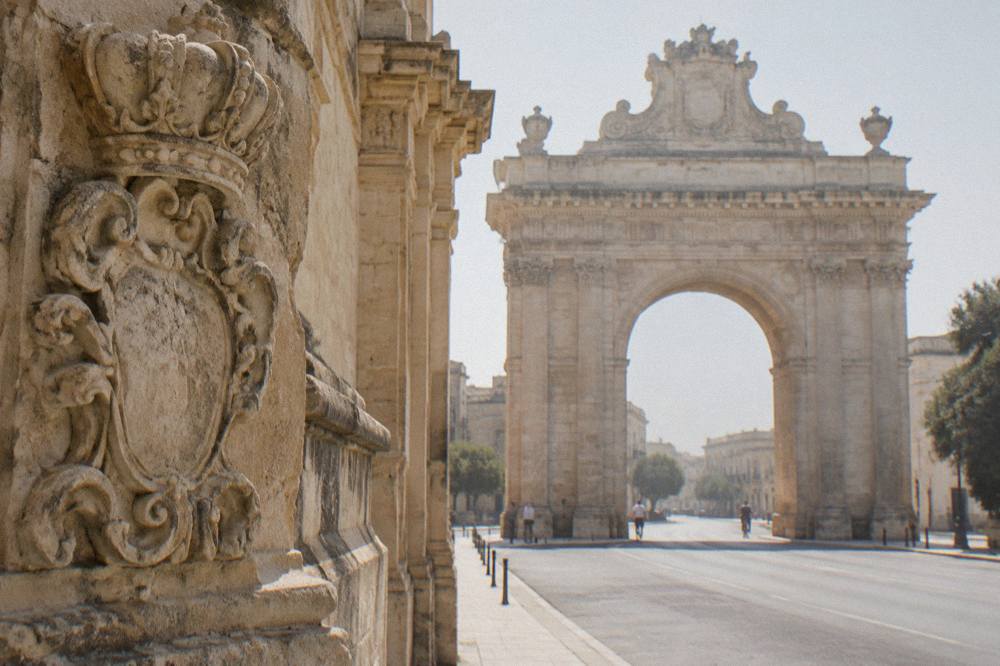 Close view of weathered limestone carving and decorative armorial detail on a monumental arch