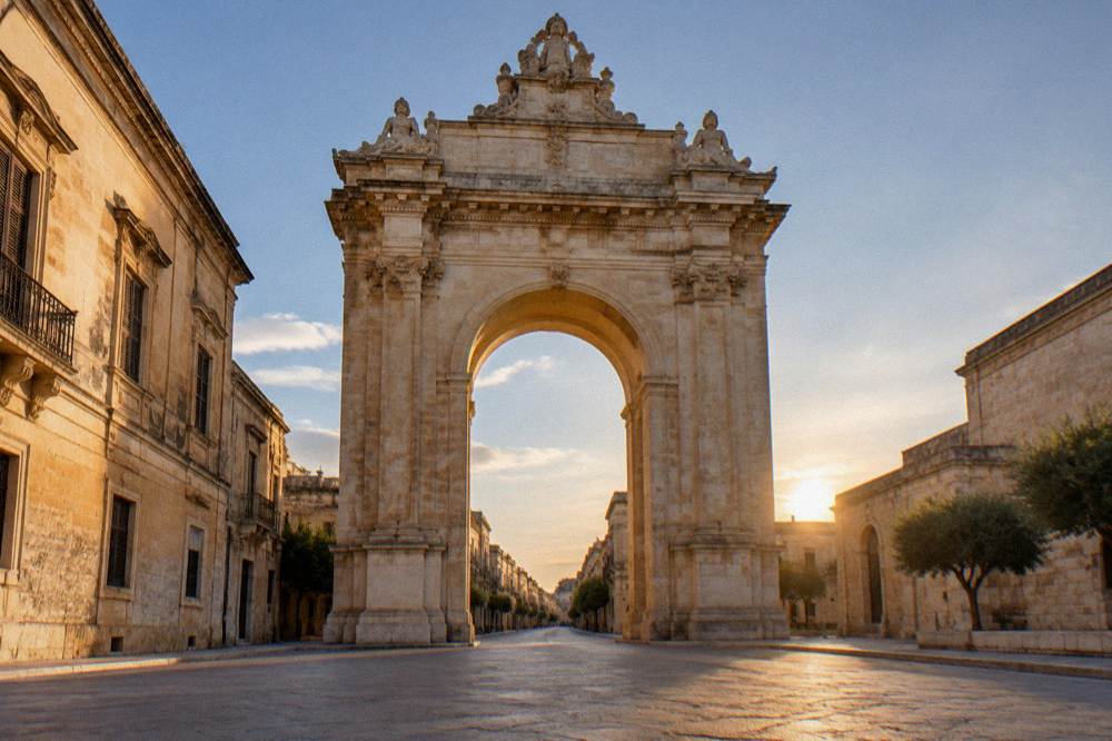 Triumphal stone arch at the end of a street, lit at dusk with no traffic in frame