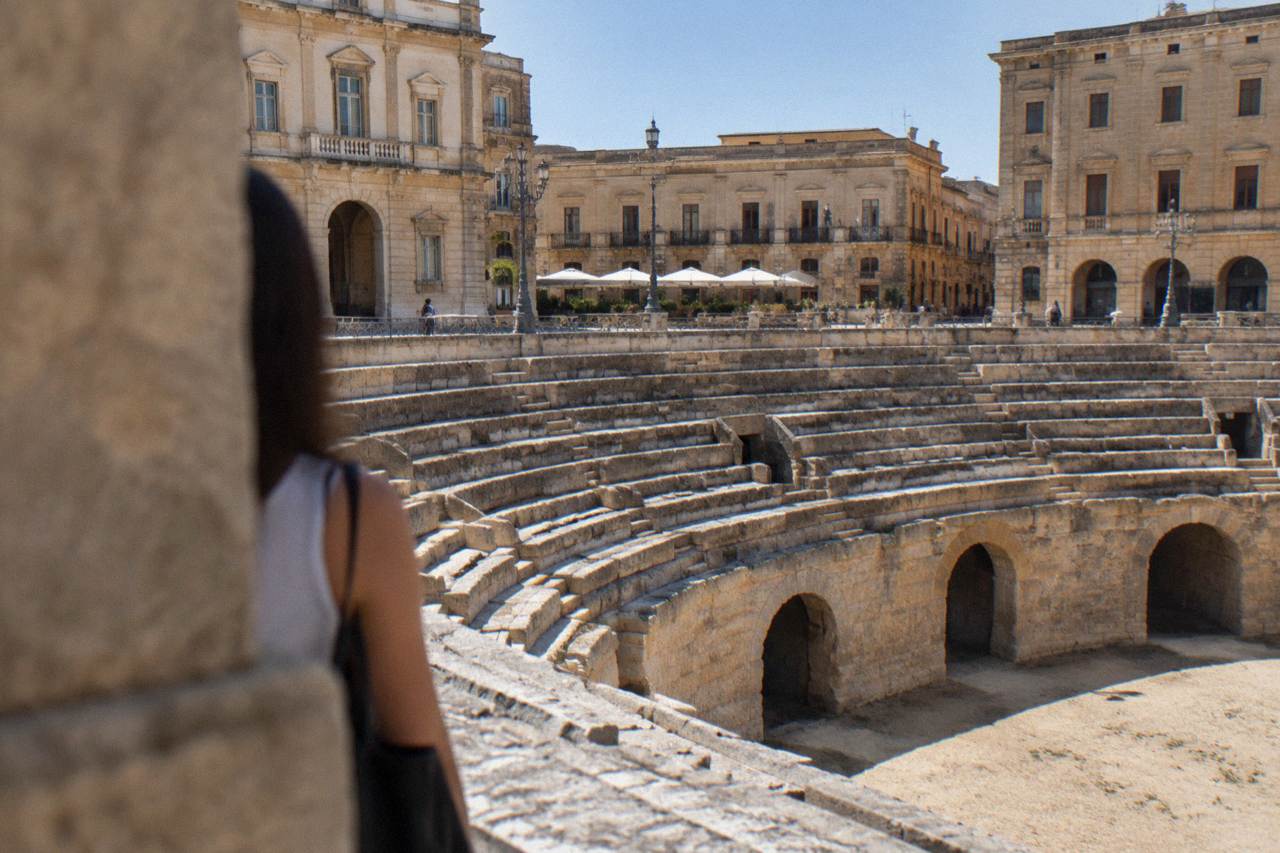 The semi-circular stone arcades of the Roman Amphitheatre sunk below the pavement of a Lecce square