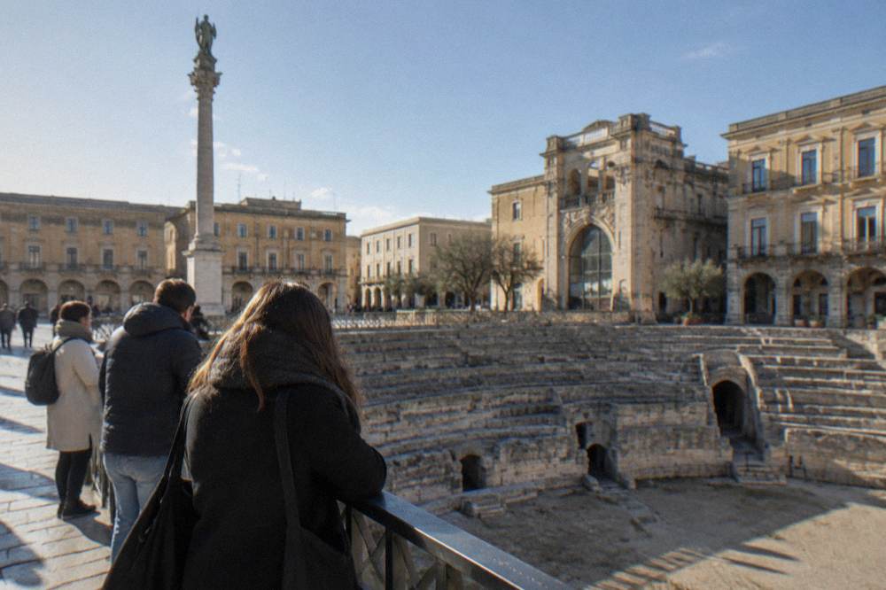 Visitors at a railing on Piazza Sant'Oronzo looking down into the sunken Roman arena