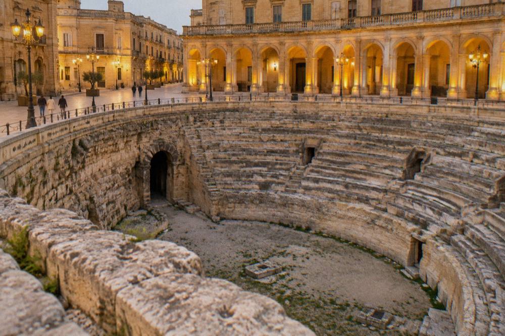 The floodlit arcades of the Roman arena seen at night from the edge of the square