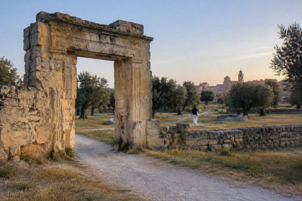 Ancient stone gate marking the entrance to a grassy archaeological site on the edge of a town