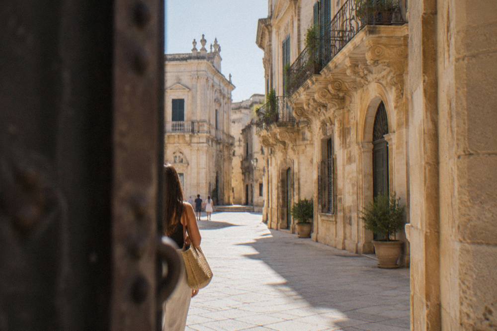 Sunlit limestone street in Lecce's old town seen from a gate, baroque facades in the distance