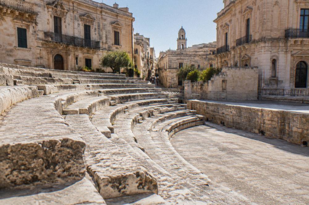 Close view of worn limestone theatre seating rows curving toward a low stage wall