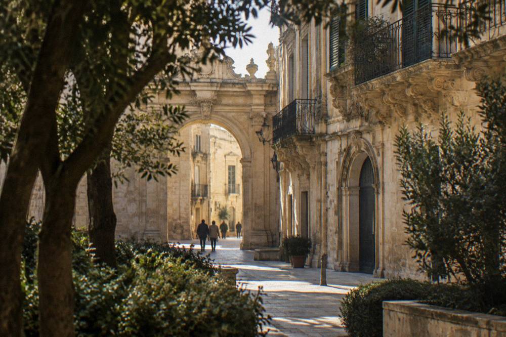 Honey-coloured baroque stone archway seen past garden trees in late afternoon light