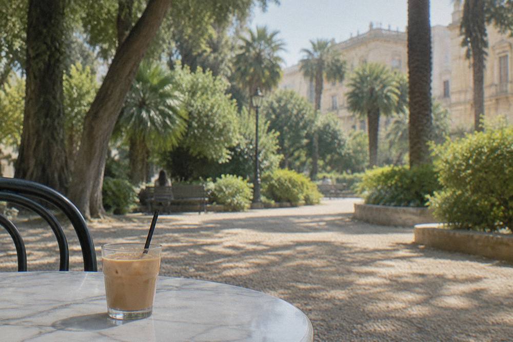 Small cup of iced coffee with almond milk on a marble cafe table in a southern Italian square
