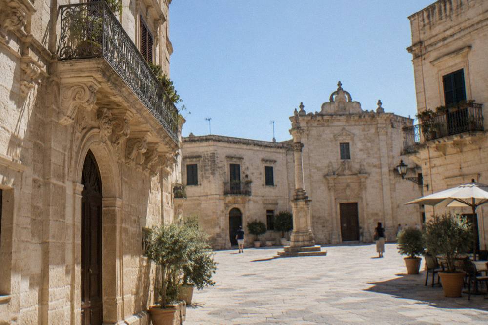 A quiet village square with pale stone buildings under a clear sky in the Lecce countryside