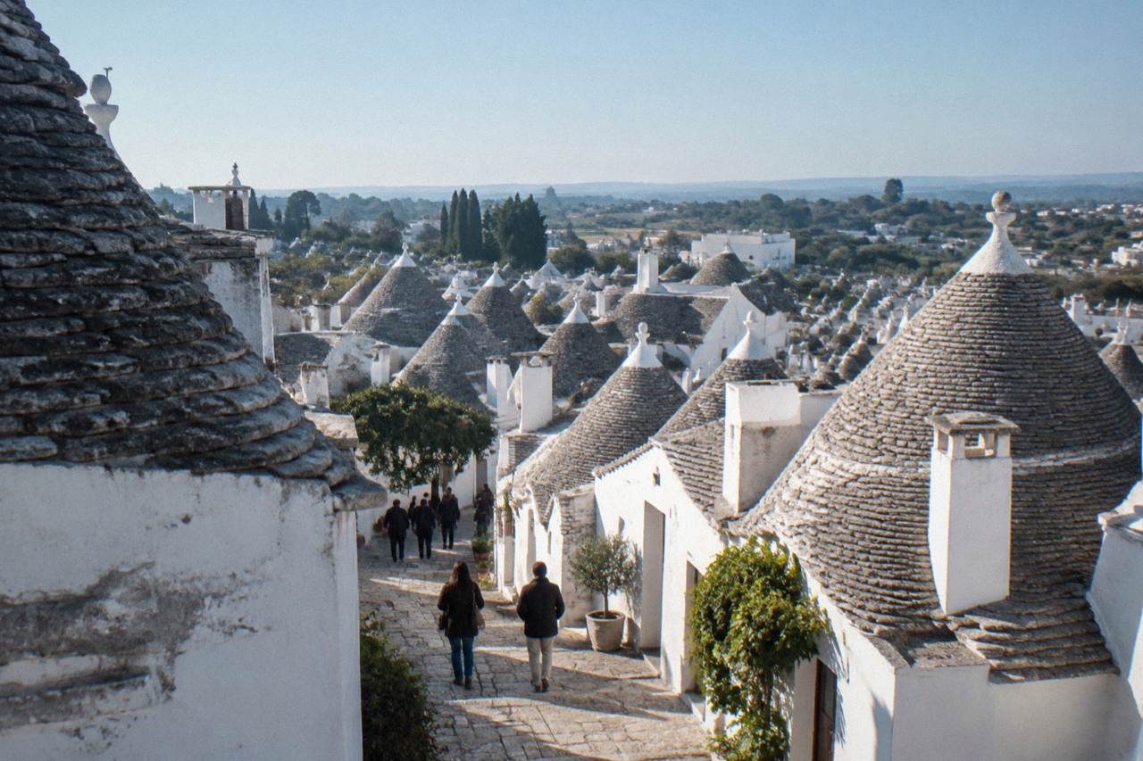 A cluster of whitewashed trulli houses with conical stone roofs under a blue sky