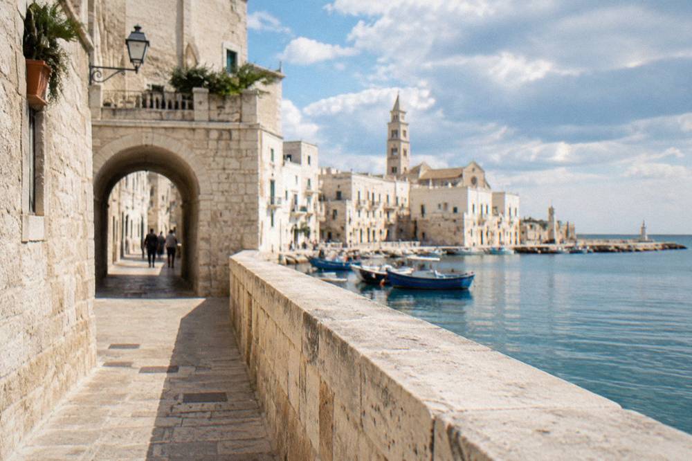View along a seafront promenade with a stone wall and calm water