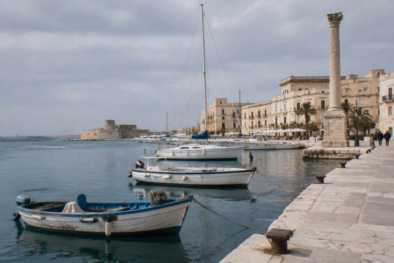 Boats moored in a southern Italian harbour with pale stone buildings along the waterfront