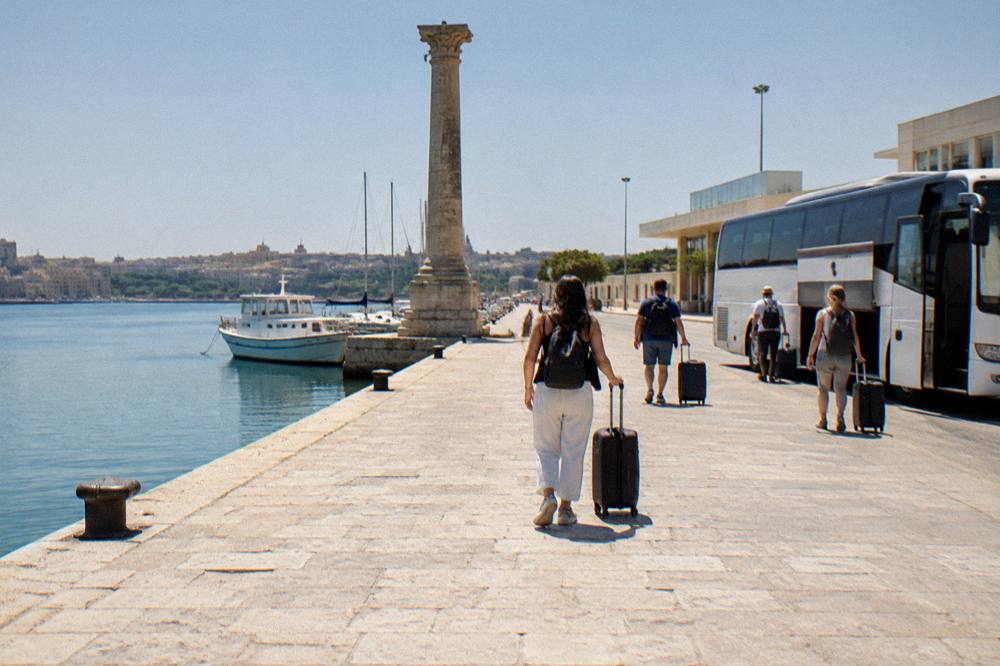 Passengers with suitcases boarding an airport shuttle bus outside a small airport terminal